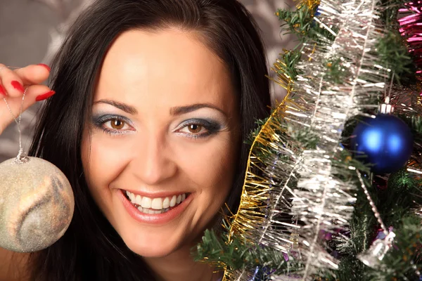 Inverno, feriados, felicidade e conceito de pessoas - mulher sorridente em santa chapéu auxiliar sobre a sala de estar com fundo de árvore de natal — Fotografia de Stock