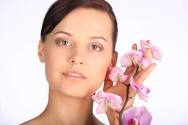 Bela cara de jovem morena com pele saudável e orquídea rosa — Fotografia de Stock