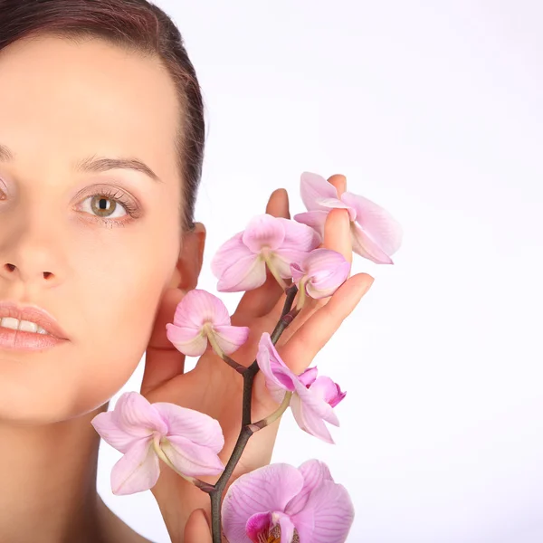 Bela cara de jovem morena com pele saudável e orquídea rosa — Fotografia de Stock