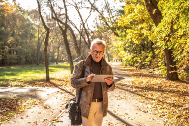 Yaşlı adam parkta dizüstü bilgisayar kullanır. Gözlüklü yakışıklı adam dışarıda çalışıyor.