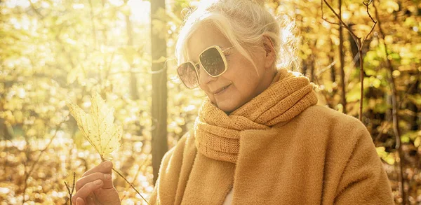 老妇人在金秋的公园里悠闲自在 手里拿着树叶 秋季活动 — 图库照片
