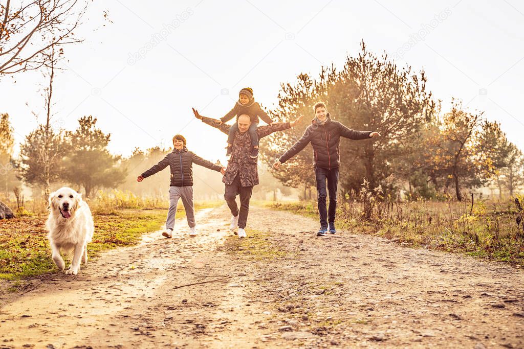 Father with three sons on a walk with goldern retriever dog in sunny beautiful autumn nature. Happy family having fun together, playing and smiling. 