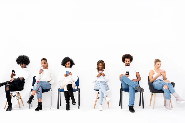 Group Multiethnic Young Friends Looking Mobile Phones Sitting Chairs Isolated — Stock Photo, Image