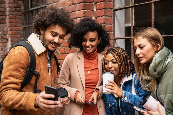 スマートフォンでソーシャルメディアで面白い写真を見ながら笑っている多民族の陽気な若い男性と女性のグループ 一緒に楽しみ 街で時間を過ごす友人 — ストック写真