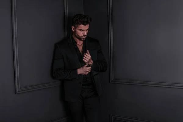 Handsome stylish man in elegant suit standing , posing on dark black background.