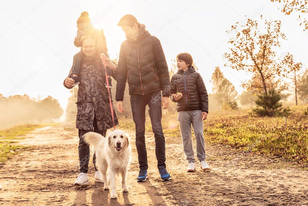 Father with three sons on a walk with goldern retriever dog in sunny beautiful autumn nature. Happy family having fun together, playing and smiling.