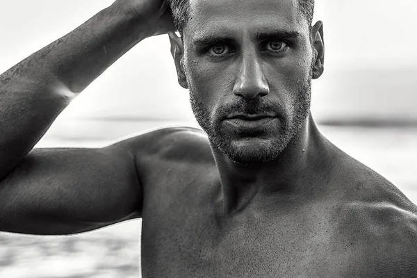 Beauty portrait of handsome, sexy italian man with beard and stunning eyes posing on the beach, sunset summer time. Tanned skin.