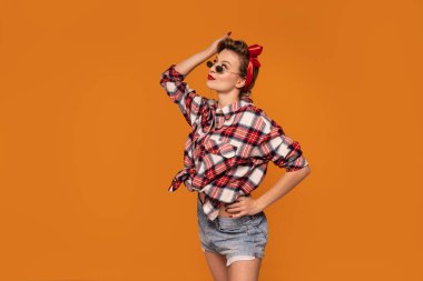 Stüdyo fotoğrafı, sarı saçlı, poster tarzı giyinmiş, poz veren, gülümseyen güzel bir genç kadın..