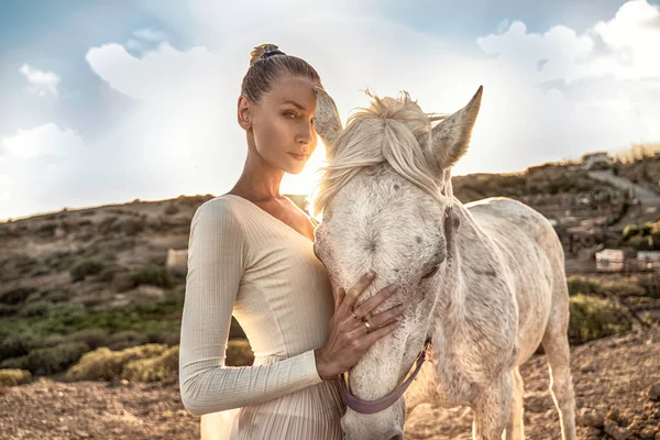 Horsewoman on rancho. Tenderness, love and animals concept. Beautiful woman touching horses foretop, looking at camera, adore spending time on the farm.