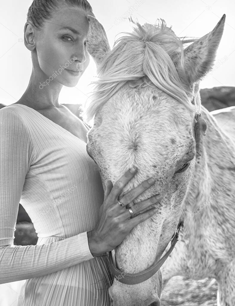 Horsewoman on rancho. Tenderness, love and animals concept. Beautiful woman touching horses foretop, looking at camera, adore spending time on the farm.