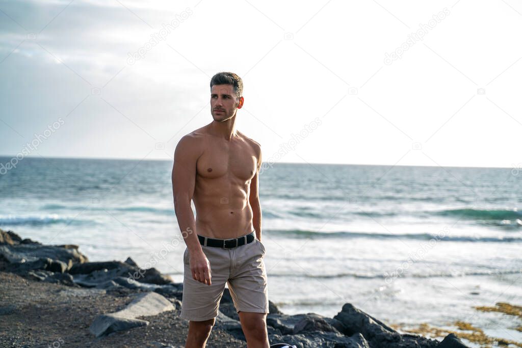 Handsome italian man posing shirtless on the beach. Muscular man outdoor. Summer vibes. 