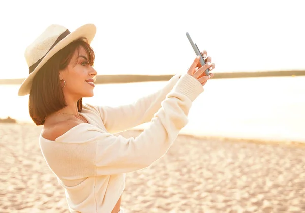 暑期海滩度假 时尚的拉丁裔女游客用智能手机拍摄有趣的手机自拍照片 戴帽子的女孩 微笑着 享受着阳光灿烂的日子 快乐生活的概念 — 图库照片