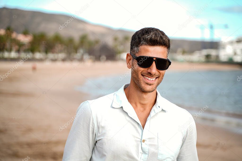 Portrait of handsome smiling italian wearing fashionable sunglasses, walking on the beach . Summer vibes.