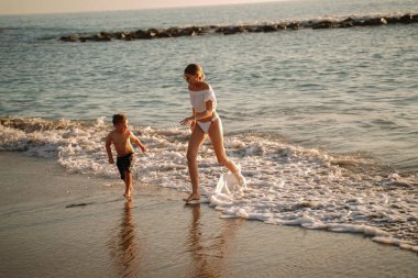 Küçük oğluyla oynayan ve gün batımında kumsalda eğlenen bir kadın. Yaz titreşimleri. Tatil kavramı.