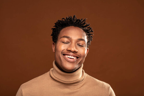 Крупный план портрета молодого счастливого африканца, улыбающегося в камеру. Браун студийный фон. Много места для копирования