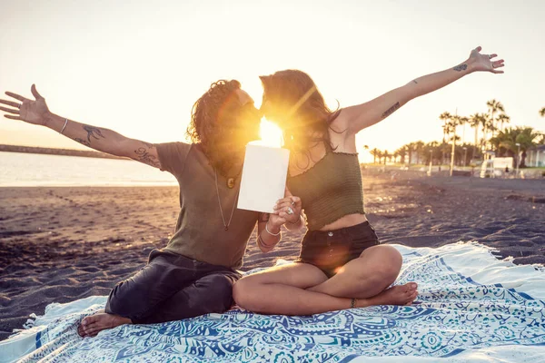 在热带海滨 一对年轻漂亮的情侣正在约会 亲吻着 展示着一本书或一张空白的白色卡片 日落时间 — 图库照片