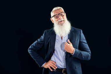 Beyaz sakallı, gülümseyen ve kameraya bakan mutlu kıdemli iş adamı. Siyah stüdyo arka planında fotokopi alanı olan yakışıklı bir yetişkin. Moda dünyasında başarılı bir yönetici.