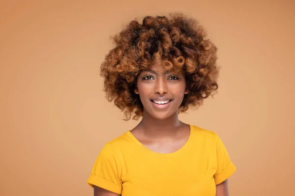 Beauty portrait of young attractive afro woman with perfect smile and delicate glamour makeup with yellow eyeliner. Girl with afro hairstyle. Studio shot. A lot of copy space.