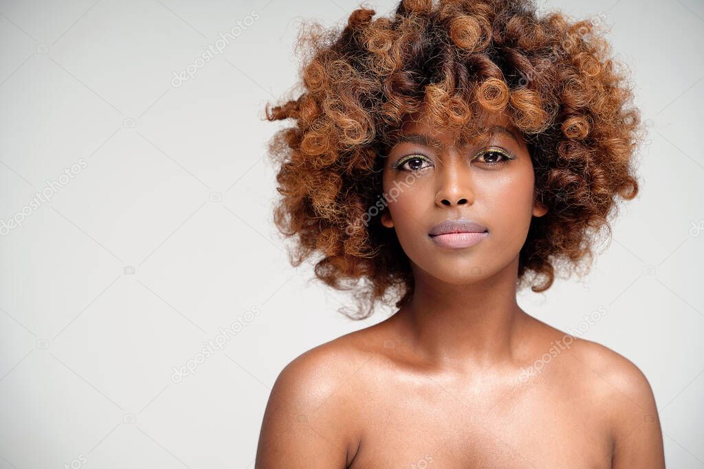Beauty portrait of young attractive afro woman with perfect skin and delicate glamour makeup with yellow eyeliner. Girl with afro hairstyle looking at camera. Studio shot. A lot of copy space.