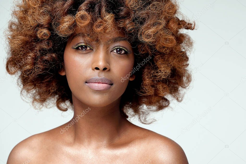 Beauty portrait of young attractive afro woman with perfect skin and delicate glamour makeup with yellow eyeliner. Girl with afro hairstyle looking at camera. Studio shot. A lot of copy space.