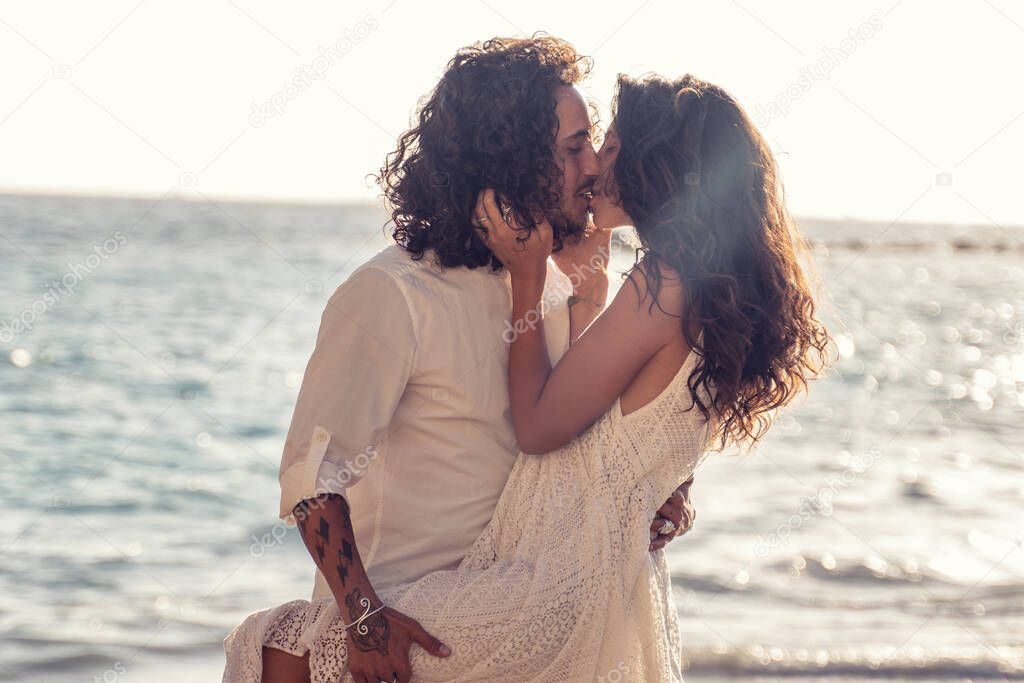 Happy cheerful couple kissing and hugging on the beach, spending time together. Island summer vibes. Romantic vacation, honeymoon love.