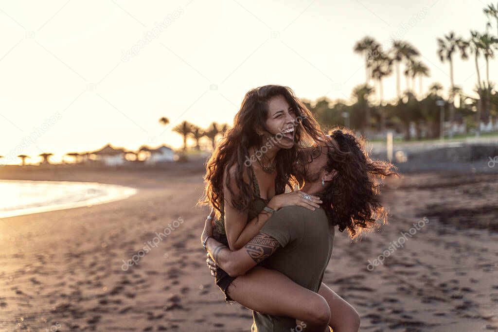 Happy beautfiul italian couple having fun together on the beach, laughing. Sunset time. Summer island vibes. Real people emotions and lifestyle. 