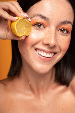 Taze limonlu doğal gülümseyen kız. Güzellik mankeni sulu meyve sıkıyor. Yüzünde doğal çiller olan neşeli bir kadın. Sağlıklı cilt bakımı kavramı, kozmetoloji.