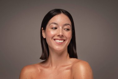 Güzel, dişlek gülümsemesi ve çilleri olan doğal bir kız. Çıplak omuzlu güzel bir genç kadının portresi. Cilt bakımı kavramı.