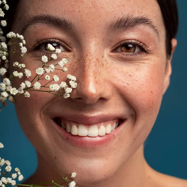 Beauty natural smiling woman with freckles, clean and healthy glowing skin. Concept of sunscreen lotions, skincare cosmetics and spa. Girl looking at the camera. Happy emotions. Small white flowers on her face. Studio shot.