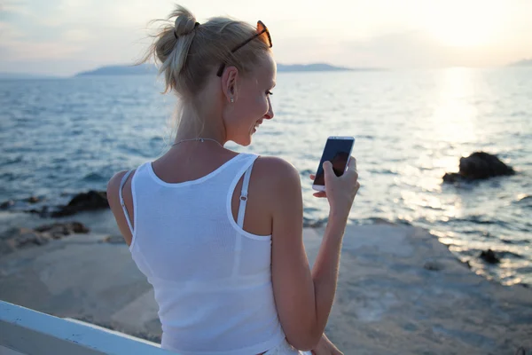 Blond kvinna med hjälp av mobiltelefon på semester. Stockbild