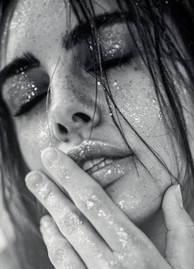 Doğal makyajı, ıslak saçı ve cildinde ışıltılı ışıltısı olan güzel bir kadının stüdyo yakın çekimi. Görüntü, şehvetli, sanatsal ve büyüleyici bir ruh halini çağrıştırıyor. Güzellik, cilt bakımı, moda veya editoryal kavramlar için mükemmel..