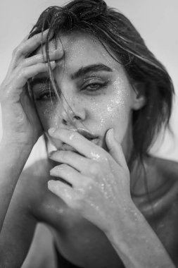 Doğal makyajı, ıslak saçı ve cildinde ışıltılı ışıltısı olan güzel bir kadının stüdyo yakın çekimi. Görüntü, şehvetli, sanatsal ve büyüleyici bir ruh halini çağrıştırıyor. Güzellik, cilt bakımı, moda veya editoryal kavramlar için mükemmel..