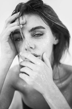 Doğal makyajı, ıslak saçı ve cildinde ışıltılı ışıltısı olan güzel bir kadının stüdyo yakın çekimi. Görüntü, şehvetli, sanatsal ve büyüleyici bir ruh halini çağrıştırıyor. Güzellik, cilt bakımı, moda veya editoryal kavramlar için mükemmel..