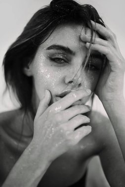 Doğal makyajı, ıslak saçı ve cildinde ışıltılı ışıltısı olan güzel bir kadının stüdyo yakın çekimi. Görüntü, şehvetli, sanatsal ve büyüleyici bir ruh halini çağrıştırıyor. Güzellik, cilt bakımı, moda veya editoryal kavramlar için mükemmel..