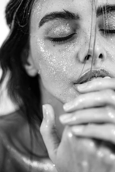 Doğal makyajı, ıslak saçı ve cildinde ışıltılı ışıltısı olan güzel bir kadının stüdyo yakın çekimi. Görüntü, şehvetli, sanatsal ve büyüleyici bir ruh halini çağrıştırıyor. Güzellik, cilt bakımı, moda veya editoryal kavramlar için mükemmel..