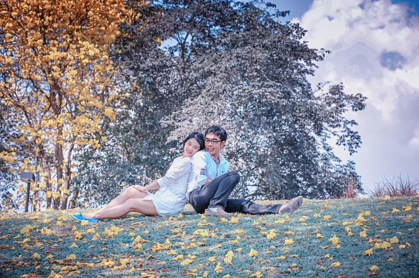 Ásia linda jovem casal back-to-back sob a árvore — Fotografia de Stock