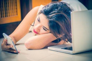 Akıllı telefon ve yerde yatarken dizüstü kullanan Asya kadın