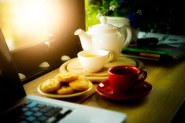 Taza de café, tetera, galletas y computadora portátil — Foto de Stock