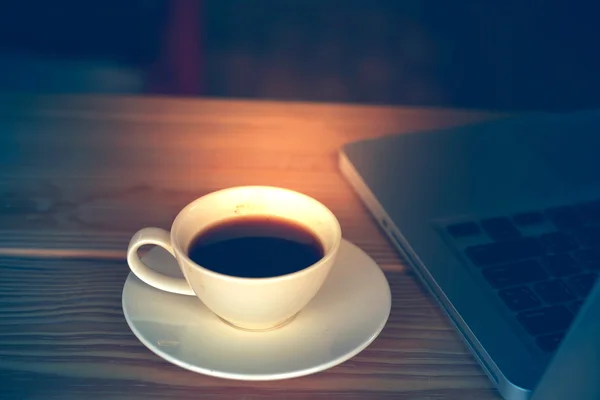 Tasse blanche de café et ordinateur portable sur table en bois . — Photo