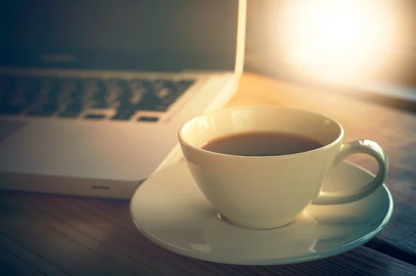Witte kopje koffie en laptop op houten tafel. — Stockfoto