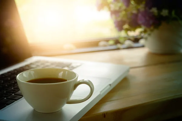Taza blanca de café y portátil en la mesa de madera . — Foto de Stock