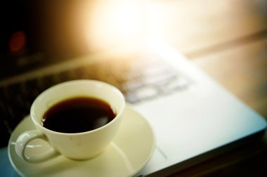 Beyaz fincan kahve ve ahşap masa üstünde laptop. 