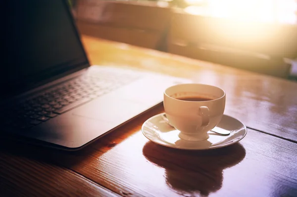 Kopje warme koffie en laptop op houten tafel — Stockfoto