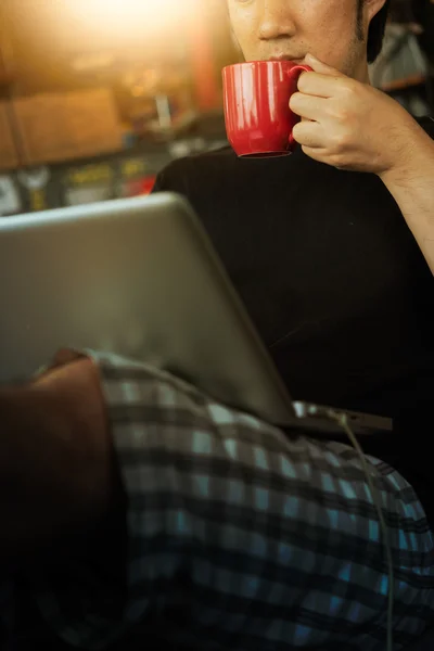 Homem usando laptop em casa com xícara de café — Fotografia de Stock