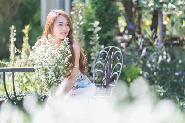 Ásia jovem mulher com flores sentado na cadeira no parque — Fotografia de Stock