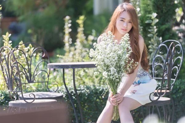 Ásia jovem mulher com flores sentado na cadeira no parque — Fotografia de Stock