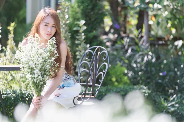 Asia giovane donna con fiori seduta sulla sedia nel parco — Foto Stock