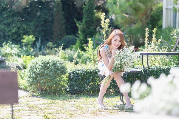 Asia giovane donna con fiori seduta sulla sedia nel parco — Foto Stock