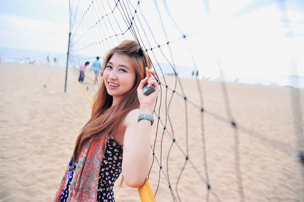 Retrato da Ásia jovem mulher perto de rede de voleibol na praia — Fotografia de Stock