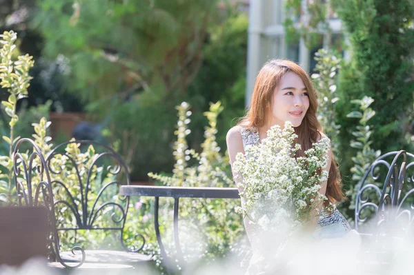 Asia mujer joven con flores sentado en la silla en el parque —  Fotos de Stock